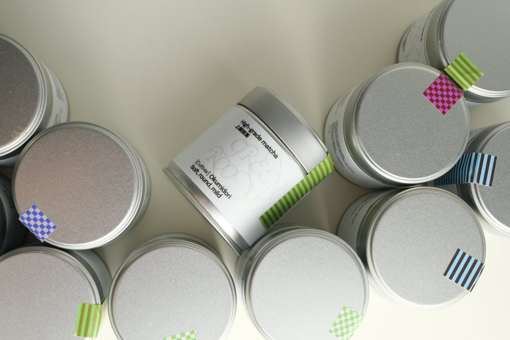 Green Room matcha tins from above with coloured labels for each cultivar, an Okumidori tin in the centre